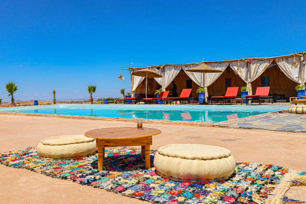 Luxury poolside seating with Moroccan poufs and colorful rug at Agafay Oasis Sky in the Agafay Desert, Morocco.