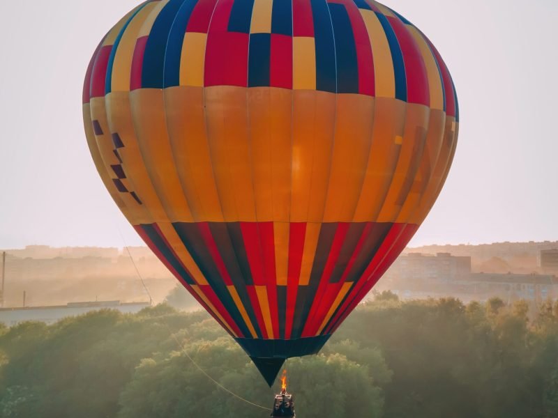 Colorful hot air balloon takes off from green park in small european city at summer sunrise, Kiev region, Ukraine